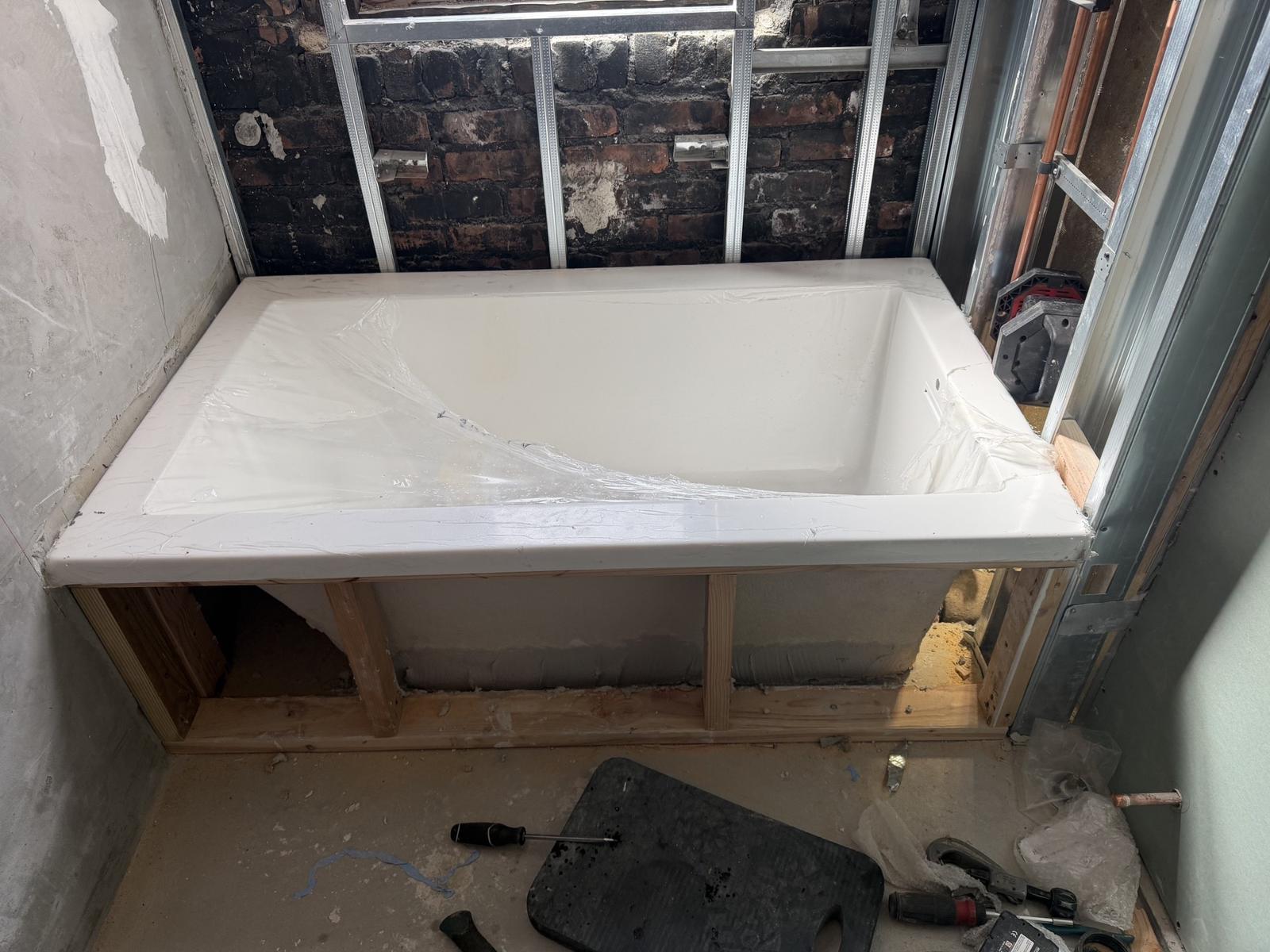 A new bathtub set on its framed platform during residential plumbing work in a Westchester home