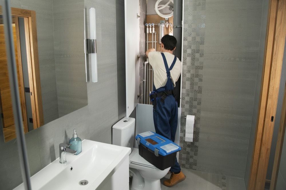 A plumber working on pipes behind a bathroom wall