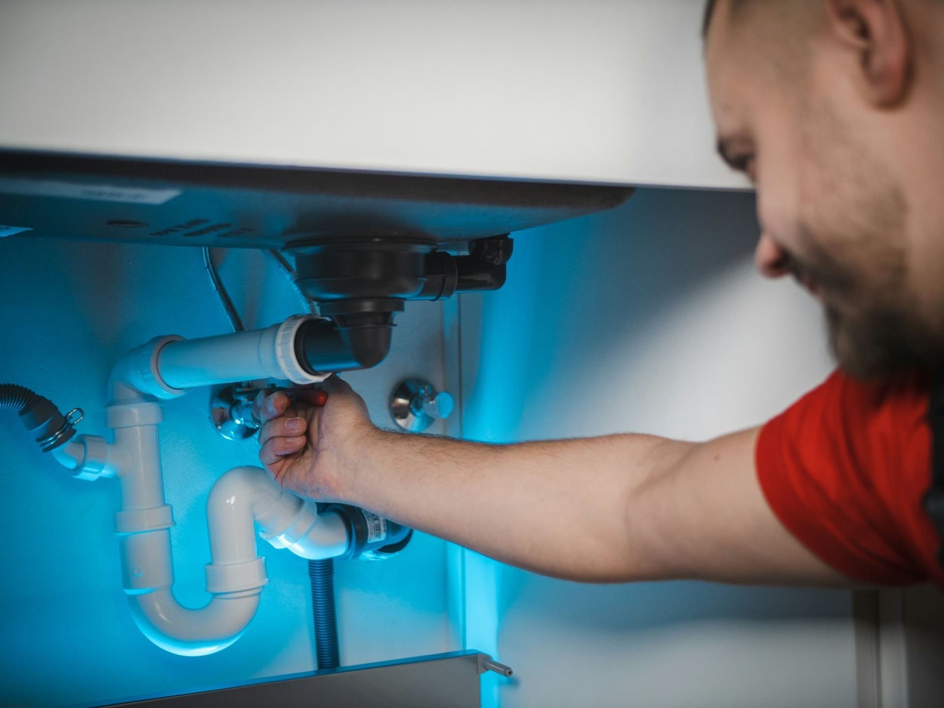 A plumber tightening the trap under a kitchen sink