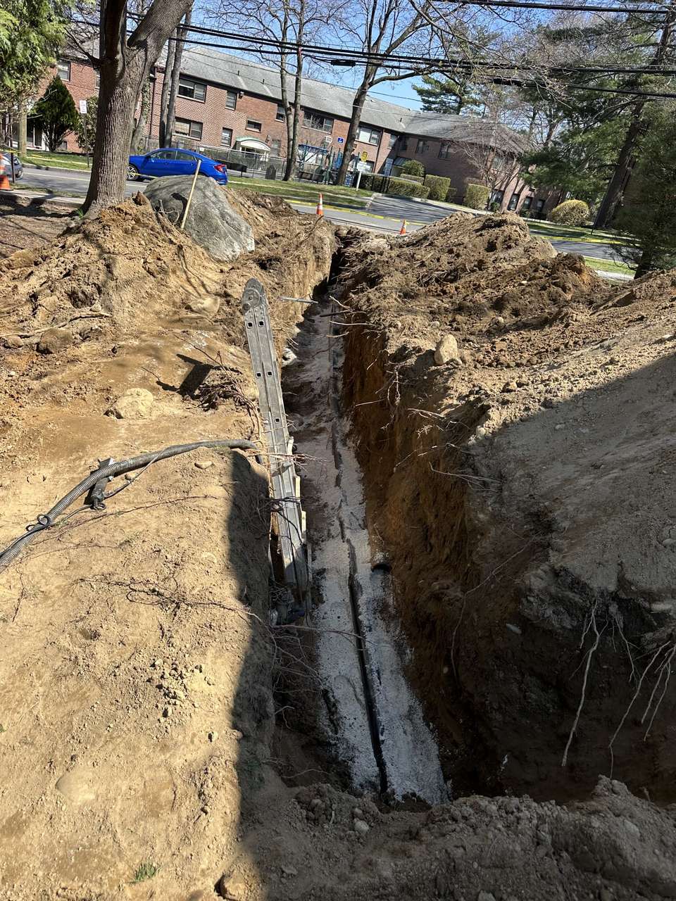An open trench across a lawn, dug to replace a blocked sewer line