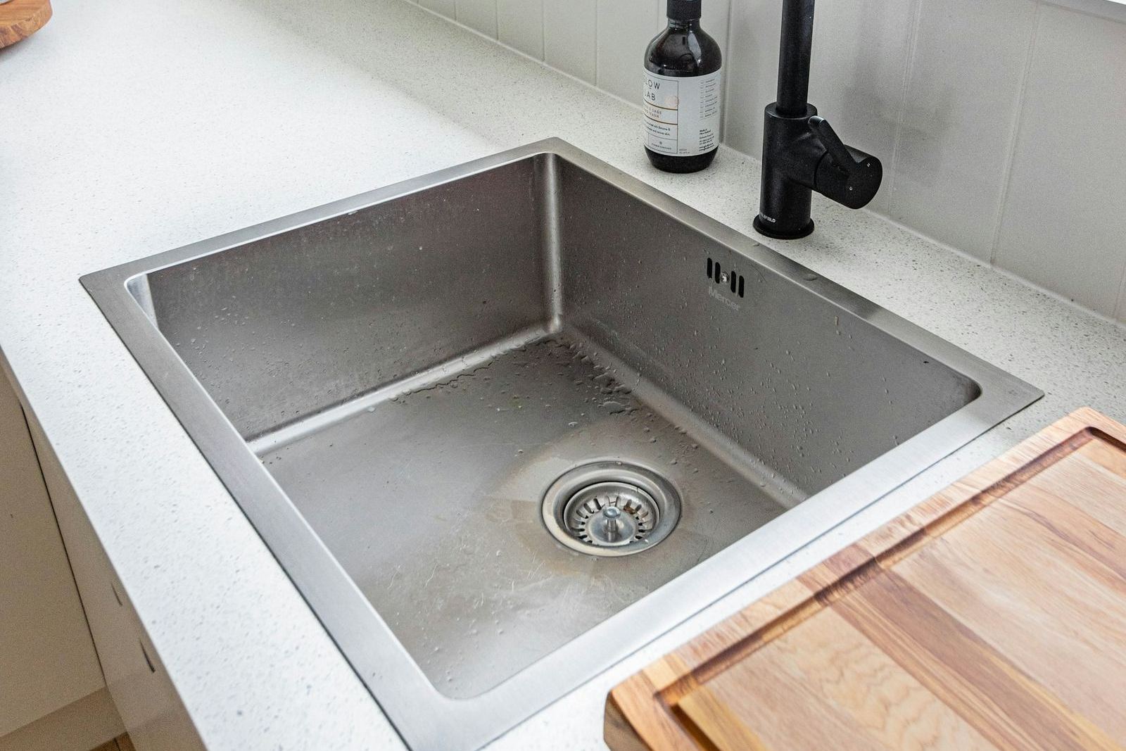 A stainless steel kitchen sink and faucet, where a garbage disposal is installed