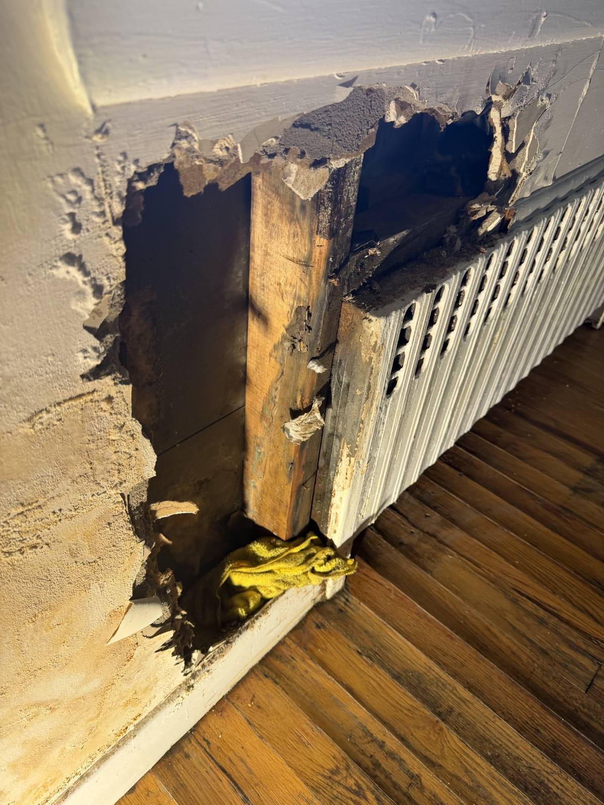 A cast iron radiator with the plaster cut back around its pipe in an older house