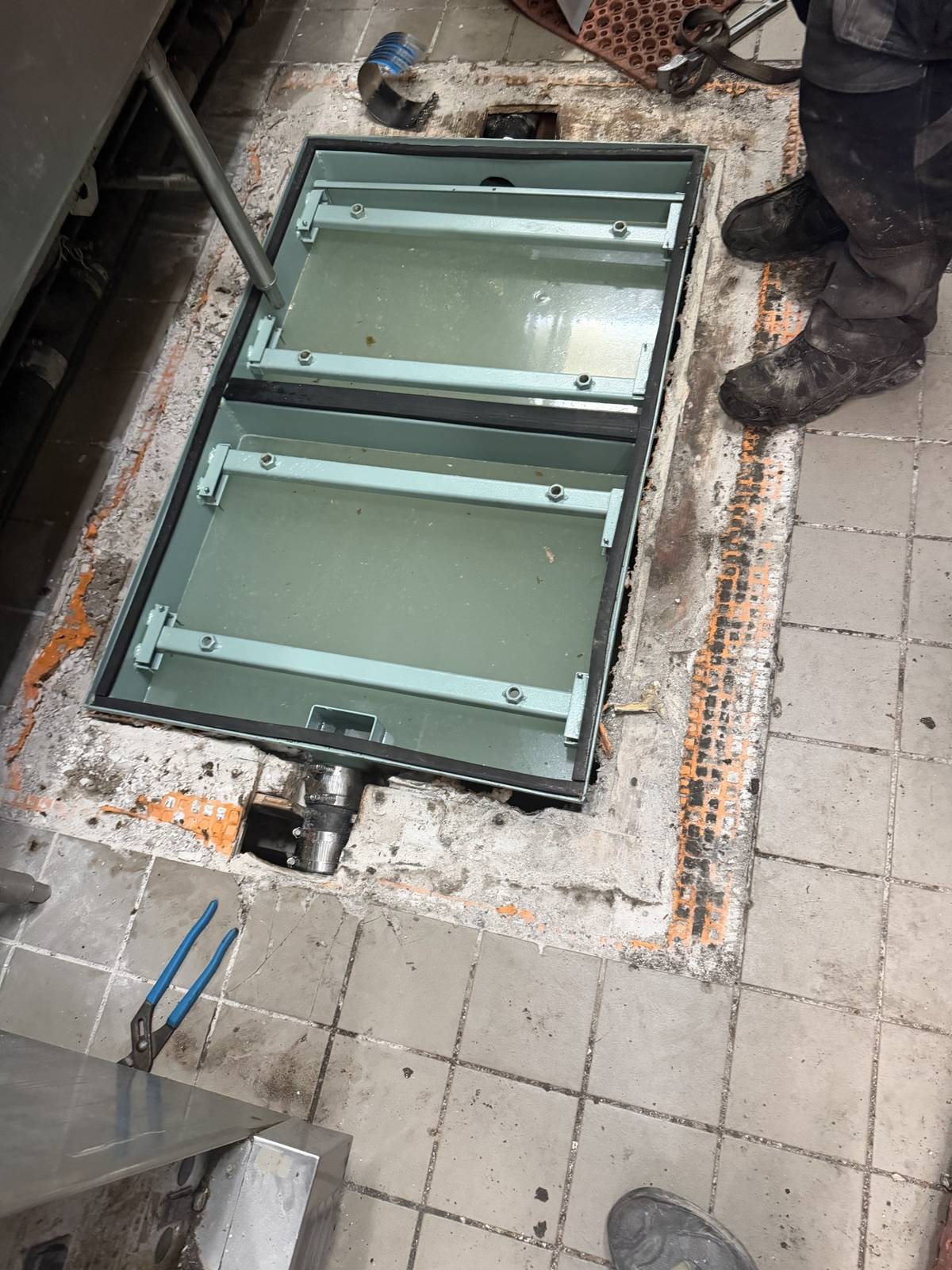 A new commercial kitchen floor hatch frame set into the floor, with the drain line below remade
