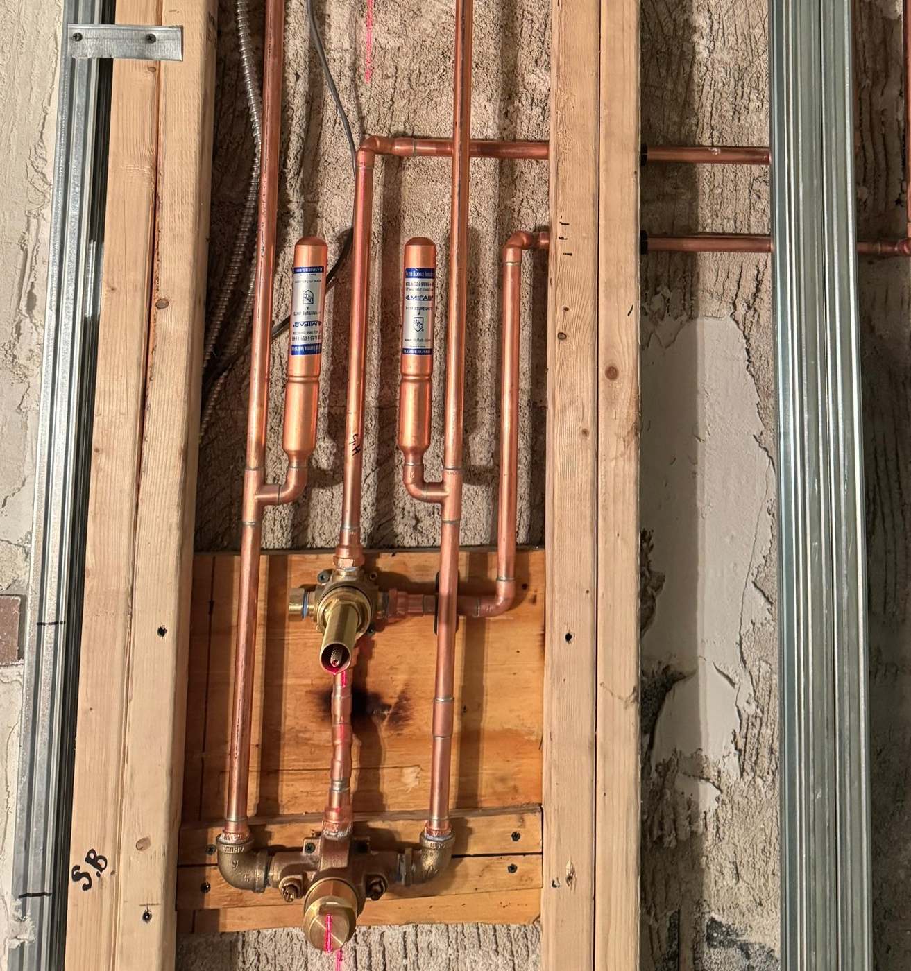 Two water hammer arrestors, the capped copper cylinders, installed above a shower valve in an open stud bay
